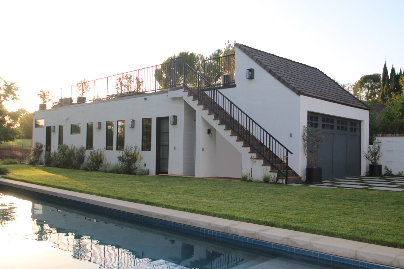 White stucco ADU with rooftop deck and exterior stair beside a pool in Hancock Park