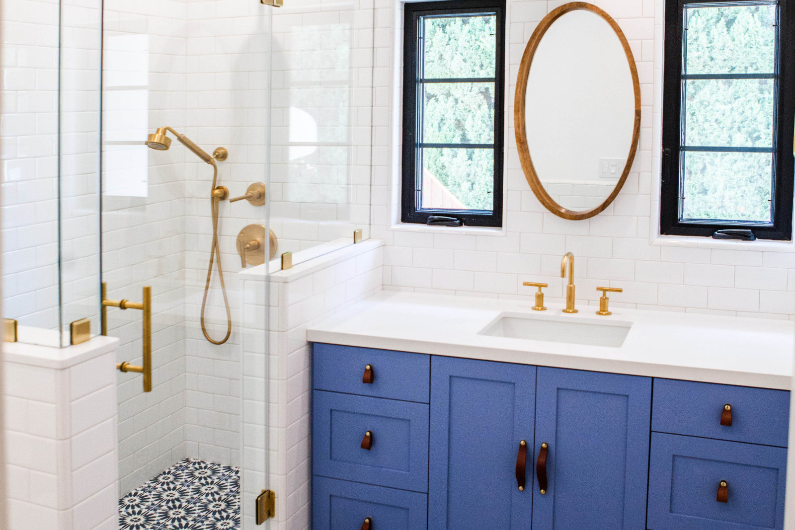 Bathroom with blue vanity, subway tile, patterned floor and brass fixtures