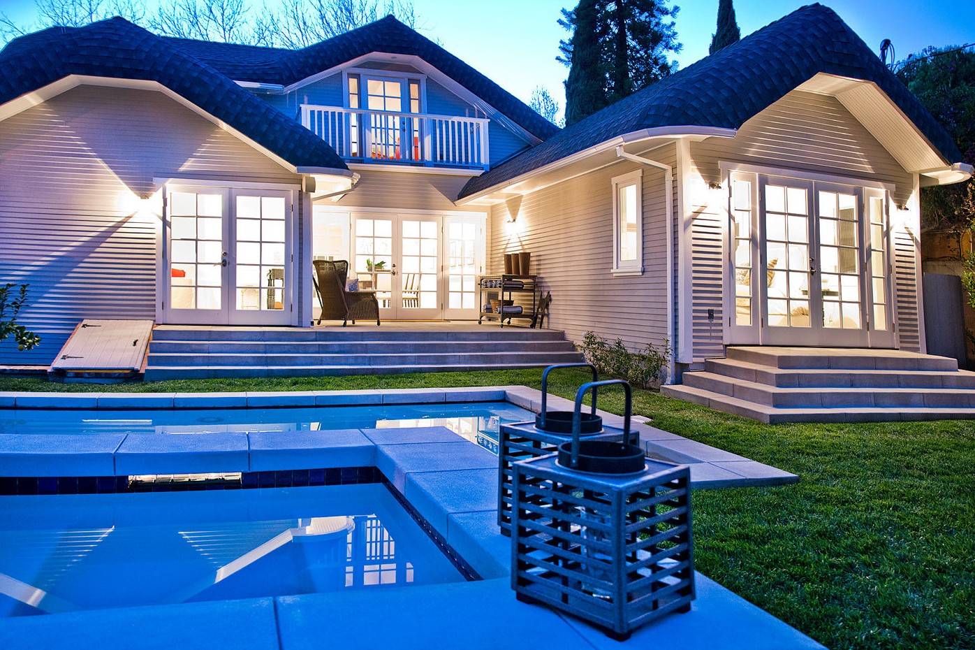 Craftsman home and guest house lit at dusk behind a pool and spa